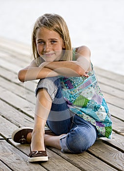 Young tween girl kneeling on a dock.