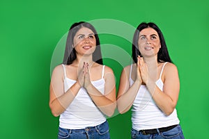 Young twin girls hold palm to palm and look up on a green background.