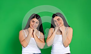 Young twin girls pose cute against green background and look tenderly into the camera