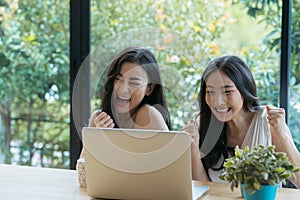 Young two Asian woman celebrating success while working on laptop at home.