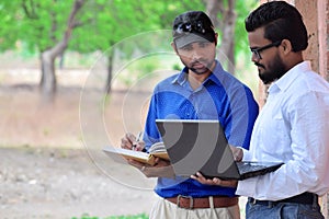 Young two Indian businessman using laptop & writing book in outdoor