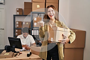 Young two people working at small business ecommerce pointing thumb up to the side smiling happy with open mouth