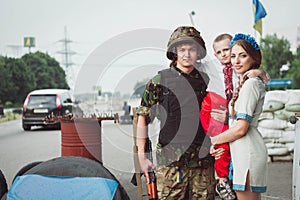 Young ukrainian woman and child boy stand near ukrainian soldier on roadblock against background of sandbags