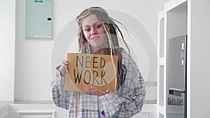 Young unemployed hipster woman with dreadlocks, in plaid shirt, fired and sad, holding cardboard poster, looking for a