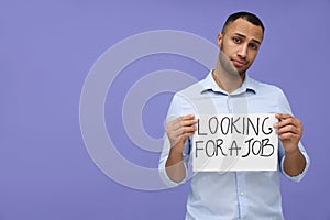 Young unemployed man holding sign with phrase Looking For A Job on violet background. Space for text