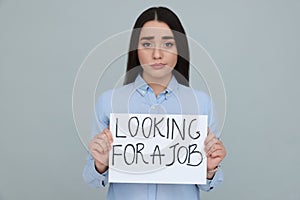 Young unemployed woman holding sign with phrase Looking For A Job on grey background