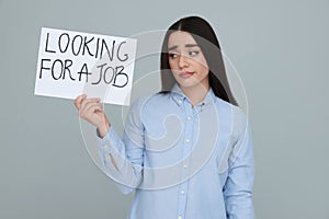 Young unemployed woman holding sign with phrase Looking For A Job on grey background