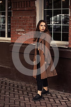 Young unhappy thinking woman walking on the street city wall background in brown coal and black shoes. Autumn season