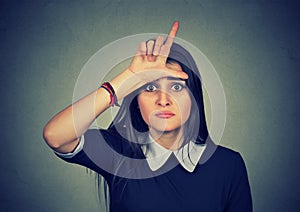 Young unhappy woman giving loser sign on forehead