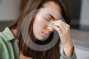 Young unhappy woman with headache holding her nose indoors