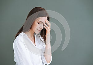 Young unhappy woman with long hair in white shirt on grey background, negative emotion