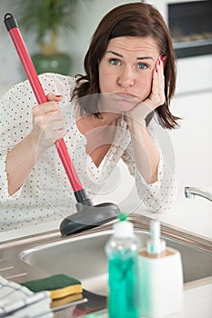 young unhappy woman using plunger in clogged sink