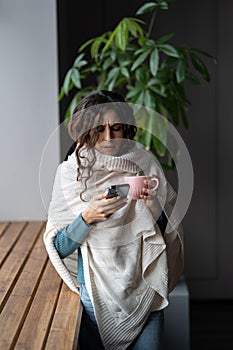 Young unhealthy woman suffering from cold or flu writing sick day email message via smartphone