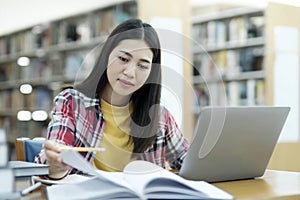 Young university student using laptop for online learning, searching and learning at library.