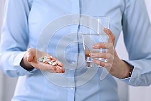 Young unknown woman holding pills and glass of water, closeup of hands. Medicine and healthcare concept