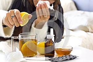 a young unrecognaseble woman with a cold opreparing tea with lemon.