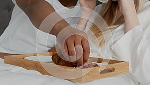 Young unrecognizable just married diverse couple eating breakfast in bed, enjoying cozy morning together