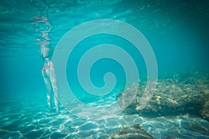 Young unrecognized woman with swimwear swimming underwater.