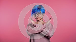 Young unusual woman with blue hair making no crossing hands sign, negation gesture over pink studio background