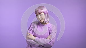 Young unusual woman with dyed violet hairstyle looking to camera, flirting. Beautiful model girl on purple studio