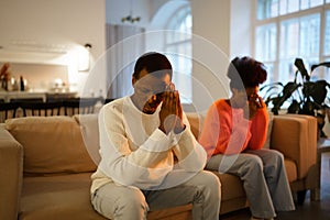 Young upset african married couple sit on sofa at home and feeling upset after quarrel