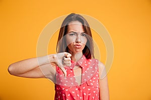Young upset brunette woman showing thumb down gesture, looking a
