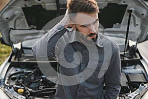 Young upset casual man trying to fix his broken car outdoors. Man waiting for towing service for help car accident on