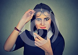 Young upset confused woman with glasses looking at mobile phone