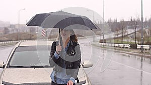 Young upset girl with an umbrella catches a car standing on the road in the rain