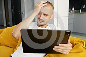 Young upset guy is browsing on his laptop, sitting at home on a cozy sofa at home. financial exchanges online.