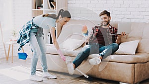 Young Upset Woman Cleaning Room with Lazy Man.