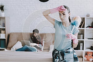 Young Upset Woman Cleaning Room with Lazy Man.