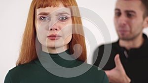 Young upset woman with red long hair is crying and young angry man is yelling behind her back.