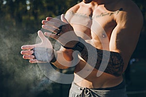 Young urban athlete with  gym grips clapping hands with magnesium chalk for calisthenics