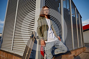 Young urban hipster guy wearing casual attire standing with skateboard