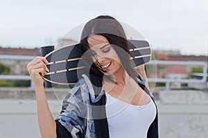 Young urban woman with closed eyes holding longboard behind head
