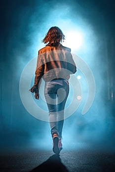 young urban woman with short red hair. leather brown jacket and light blue jeans. back light in a urban street at night.