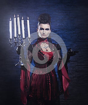 A young vampire lady in a dress holding candles