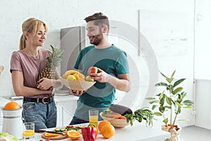 young vegan couple with fresh fruits and vegetables in kitchen