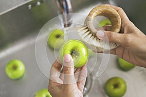 Young Vegan Girl Washing Green Apples with Bamboo Brush. Hand Holding Fresh Fruits Under Running Water in Kitchen Sink