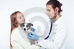 Young veterinarian doctor in blue gloves examine little cute dog jack russell isolated on white background with owner