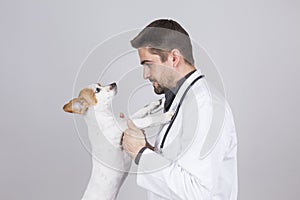 Young veterinarian man examining a cute small dog by using stethoscope, isolated on white background. Indoors