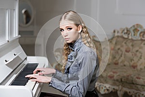 Young Victorian girl in a tender blue dress learning to play piano. Lovely blond with curly hair woman sitting in room