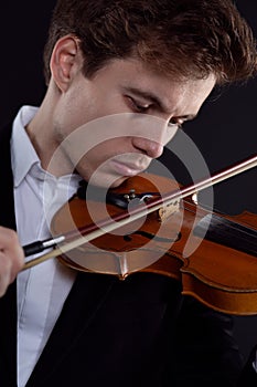 Young violinist playing an old instrument on a dark background, close-up portrait