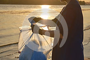 Young volunteer in black gloves is walking with garbage bag along a dirty beach of the river and cleaning up trash