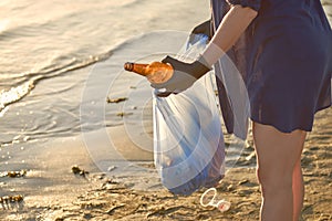Young volunteer in black gloves is walking with garbage bag along a dirty beach of the river and cleaning up trash