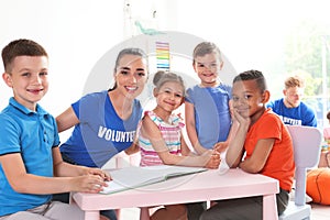 Young volunteer reading book with children at table