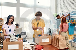 Young volunteers group sorting, packing food and clothes in cardboard boxes, Diverse team working on donation project