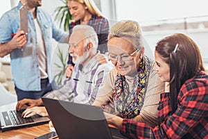 Young volunteers help senior people on the computer.