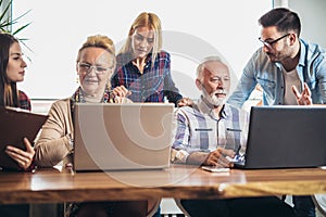 Young volunteers help senior people on the computer.